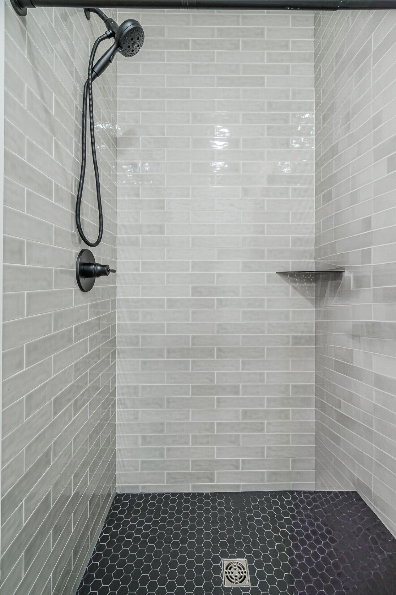 A shower area with a black hose and a showerhead, tiled walls, and a hexagonal patterned floor.