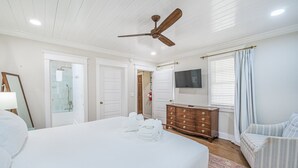 A bedroom with a large bed, a wooden dresser, a ceiling fan, a TV on the wall, and a window with curtains. - The Bogard Only 4 Blocks to King! Unit A (Charleston)