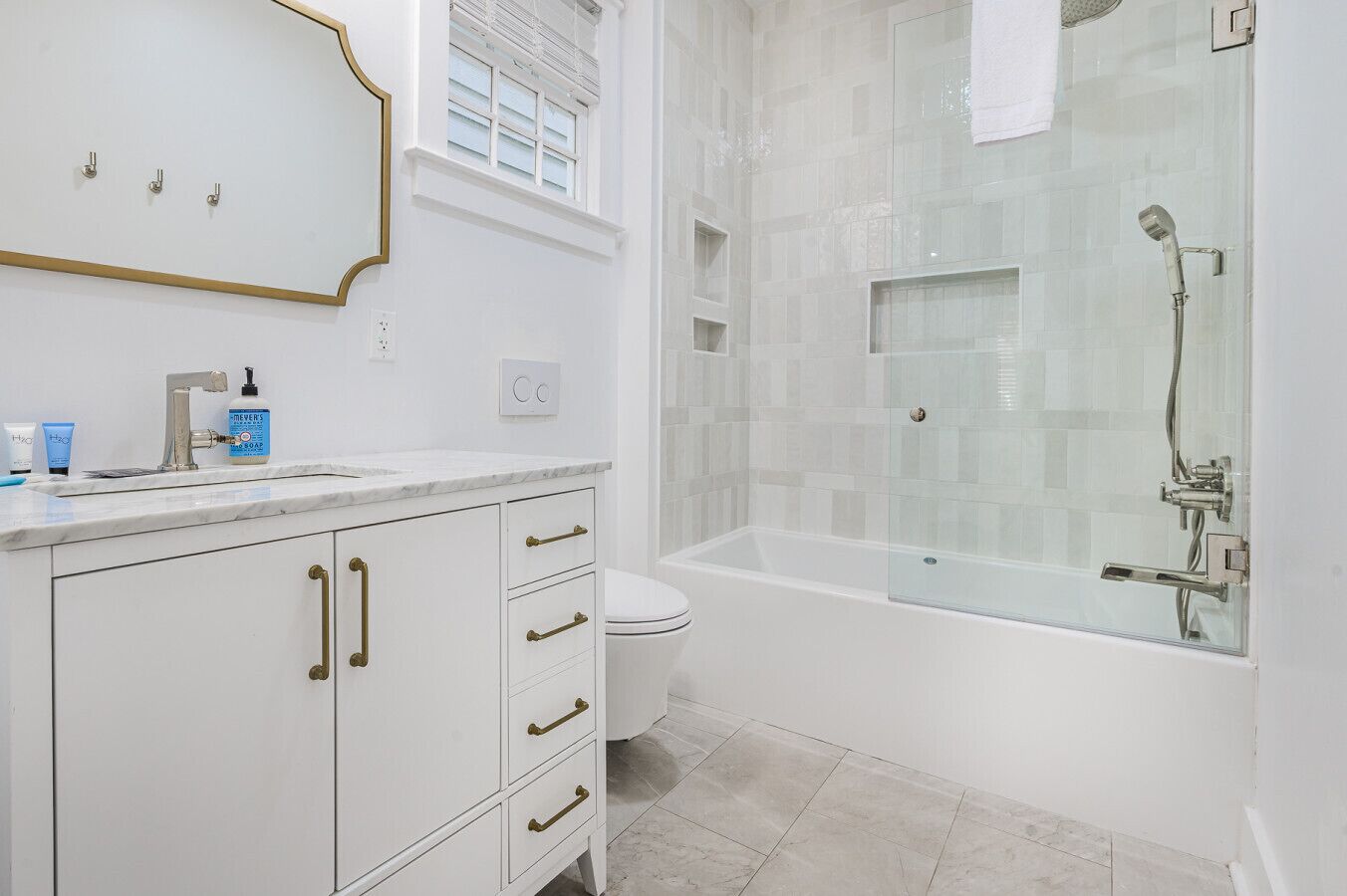 A modern bathroom with a glass-enclosed shower, white cabinetry, and a marble countertop.