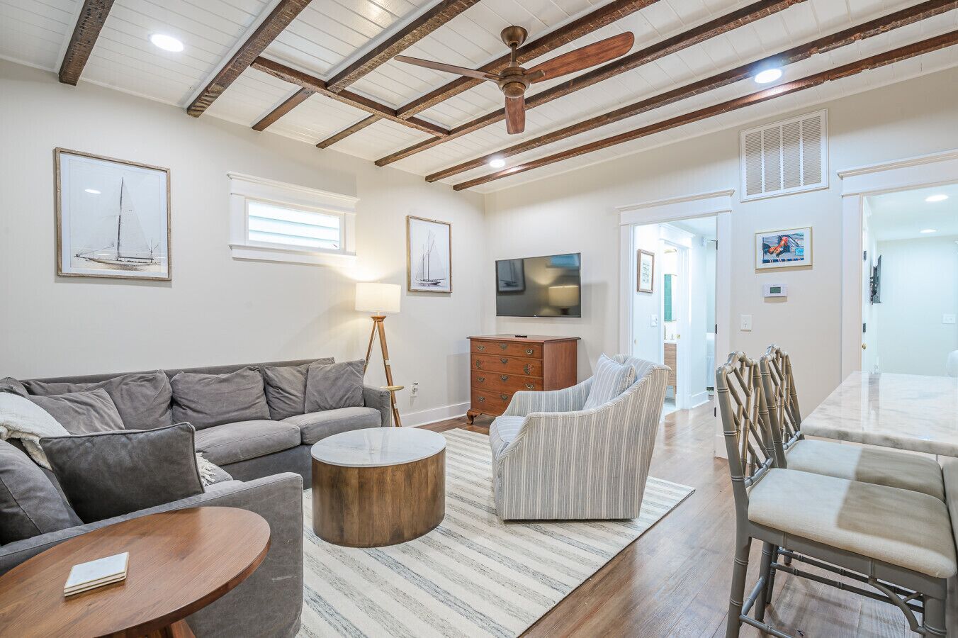 Amplia sala de estar con un sofá gris, una mesa de centro redonda de madera, un sillón a rayas y una zona de comedor con mesa y sillas.