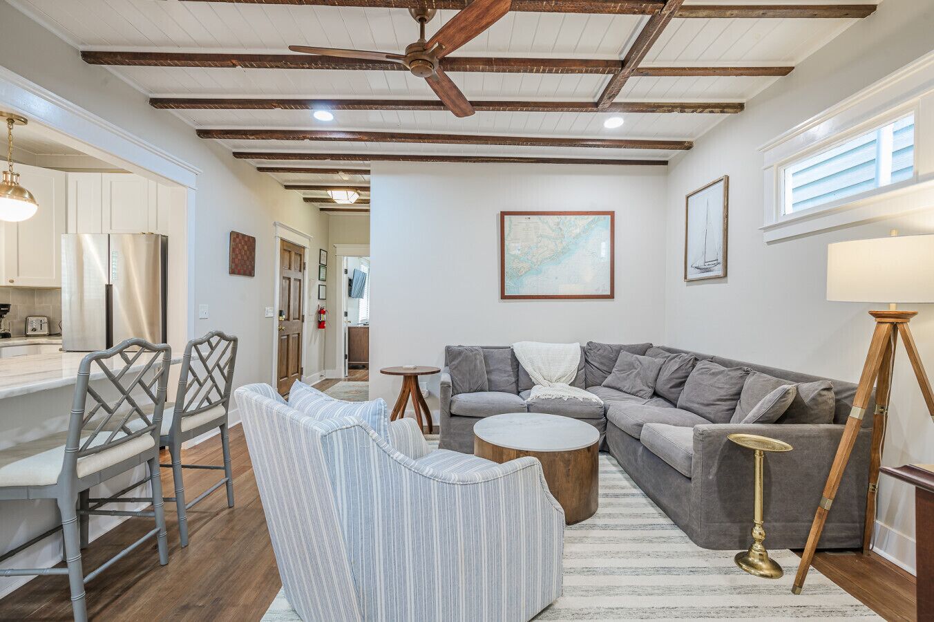 A modern living room with a gray sectional sofa, a round coffee table, and striped chairs. There is a wooden ceiling with exposed beams and a ceiling fan.
