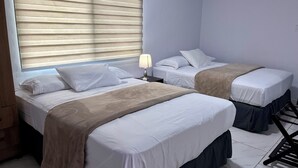 A hotel room with two beds, a nightstand with a lamp, and a window with blinds.