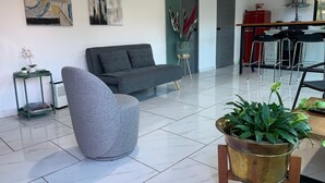 A modern living room with a grey sofa, a round grey chair, and a large potted plant.