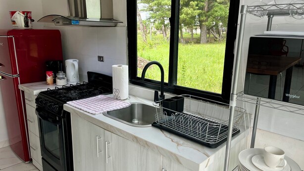 A kitchen with a sink, stove, and a window overlooking a grassy area.