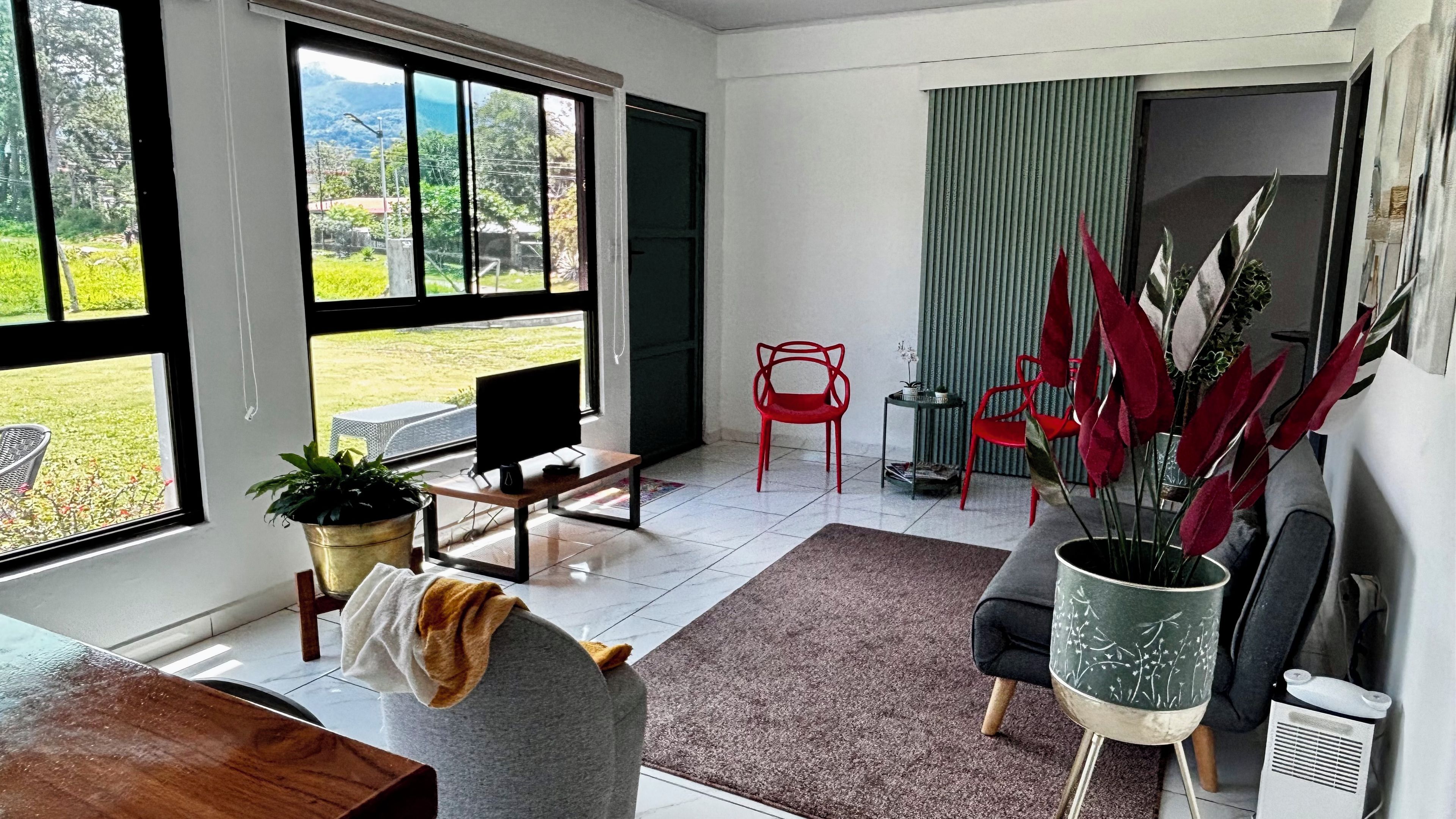 A modern living room with a large window, a dining area, and a red chair.