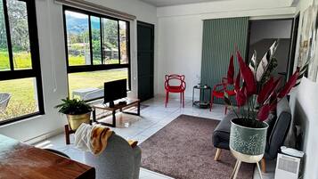 A modern living room with a large window, a dining area, and a red chair.