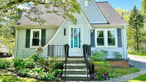 A two-story house with a front porch, a mailbox, and a small garden with various plants.