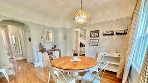 A dining area with a round wooden table, white chairs, and a hanging light fixture.