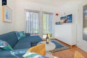 A living room with a blue sofa, a small round table with a bottle and glasses, a white cabinet, and a painting of a ship on the wall.