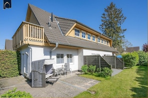 A two-story house with a sloped roof, a balcony, and a small patio area with outdoor furniture.