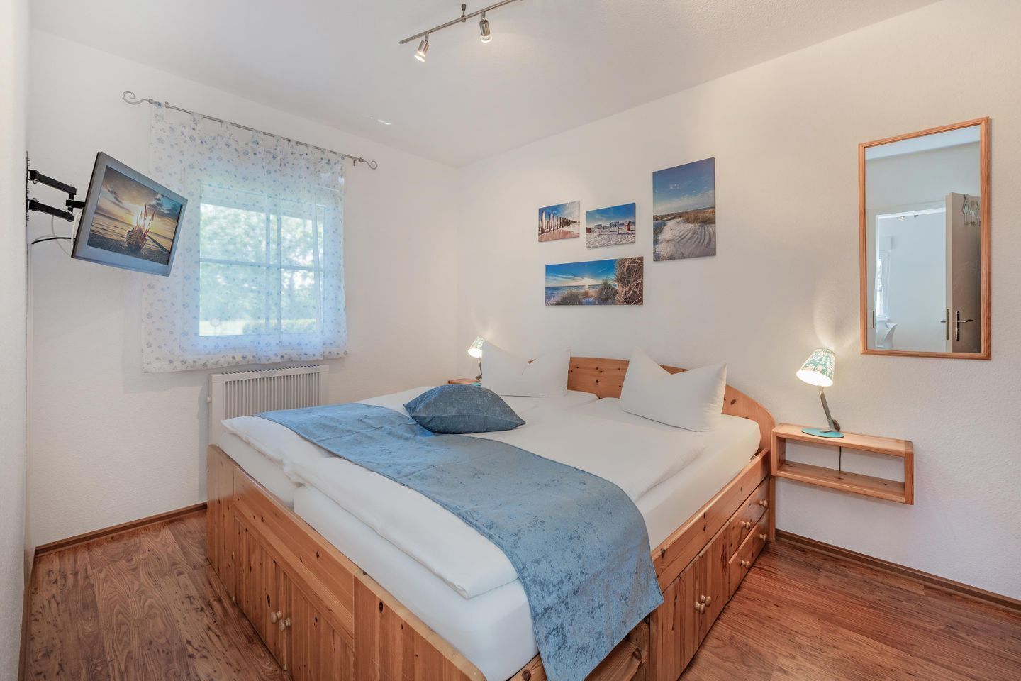 A bedroom with a bed, bedside lamps, a mirror, and wall art.