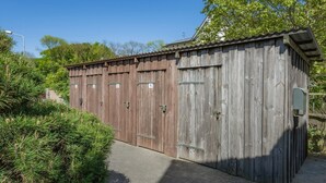 Un bâtiment en bois avec des portes numérotées, une entrée pavée et de la verdure tout autour.