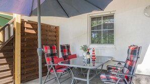 Une terrasse avec une table et des chaises en verre, une bouteille de vin et une plante en pot.