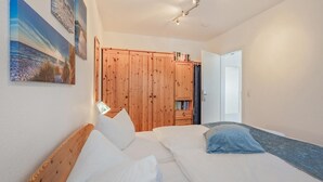 A bedroom with two beds, wooden wardrobe, and a door leading to another room.