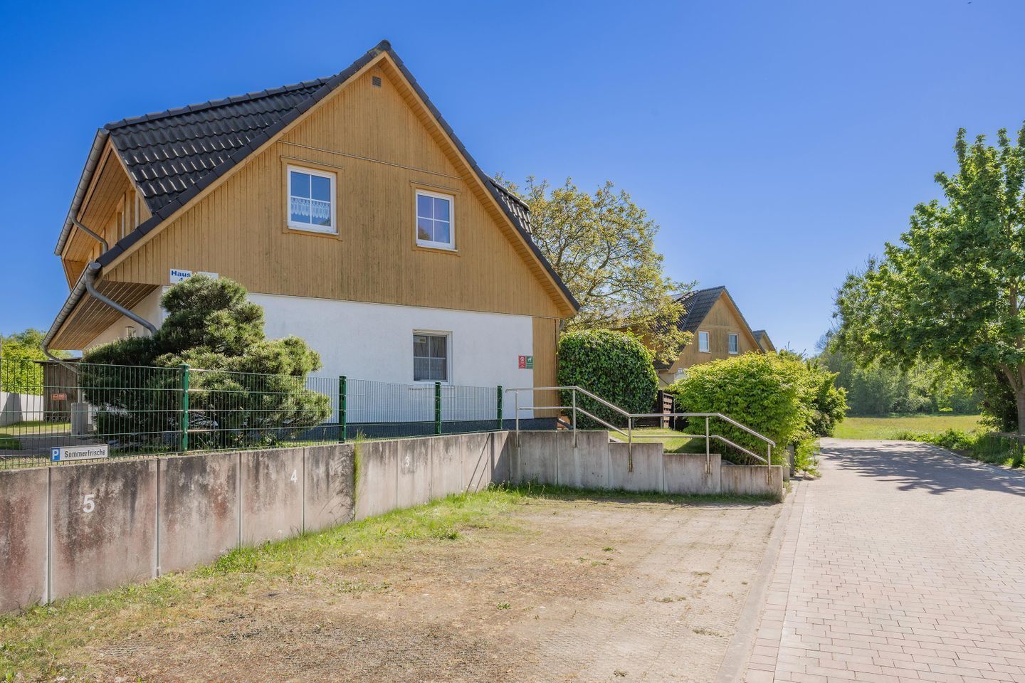 Ein zweistöckiges Holzhaus mit geneigtem Dach, einer kleinen Veranda und einer gepflasterten Auffahrt zu einem verschlossenen Eingang.