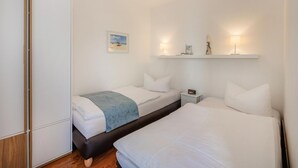 Une chambre d’hôtel avec deux lits, une armoire, des tables de chevet et des lampes fixées au mur.