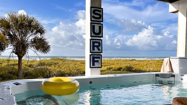A pool with a view of the ocean, a palm tree, and a 'SURF' sign. - Oceanfront 5BR Hot Tub & Swim Spa (Galveston)
