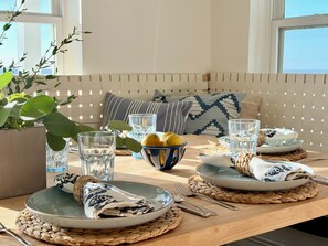 Un comedor con una mesa de madera dispuesta para dos personas, con individuales tejidos, platos, cubiertos y vasos.