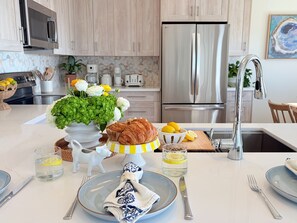 Una cocina moderna con un refrigerador de acero inoxidable, un microondas y un lavamanos. Hay un florero con flores en la encimera, un plato con servilleta y un vaso de agua.