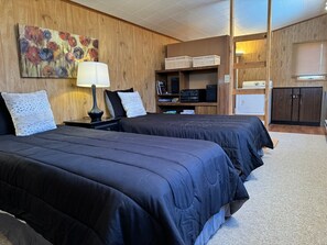A hotel room with two beds, a wooden wall, a painting, a lamp, a TV, and a kitchenette. - Loren's Lookout- pet friendly, on the way to Yellowstone National Park (Cody)