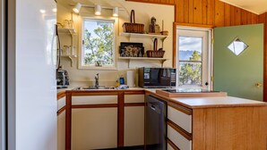 A compact kitchen with wooden cabinetry, a built-in microwave, and a window with a view of trees and mountains. - Loren's Lookout- pet friendly, on the way to Yellowstone National Park (Cody)