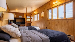 A cozy room with two beds, a desk with a lamp, a shelf with books and electronics, and large windows with a view. - Loren's Lookout- pet friendly, on the way to Yellowstone National Park (Cody)