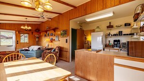 A cozy cabin interior with a wooden dining area, a kitchen with a refrigerator, and a living room with a sofa and a lamp. - Loren's Lookout- pet friendly, on the way to Yellowstone National Park (Cody)