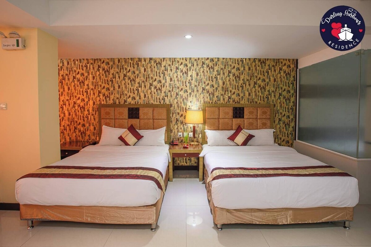Une chambre d’hôtel avec deux lits, un mur décoré d’un motif, une table de chevet avec une lampe et une grande fenêtre.