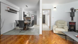 A modern living room with a herringbone wood floor, a dining area with a table and chairs, a beige armchair, and a wood-burning stove. - House Ada (Istria - Poreč) (Poreč)
