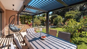 A covered patio area with a table, chairs, a hanging chair, and a garden view. - House Ada (Istria - Poreč) (Poreč)