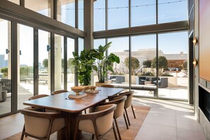 Uma área de jantar moderna com uma mesa grande e cadeiras, janelas amplas e vista para o exterior.