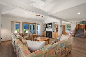 A spacious living room with a fireplace, wooden furniture, and large windows.
