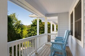 A covered porch with white railings and blue chairs, overlooking a forested area. - Cloudbreak: Pet Friendly, Oceanside, Hot Tub, Community Amenities! (Duck)
