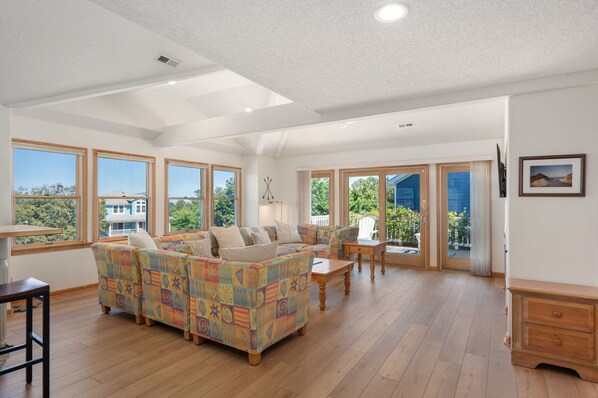 A spacious living room with a large sofa, a dining table, and a view of the outdoors through large windows.