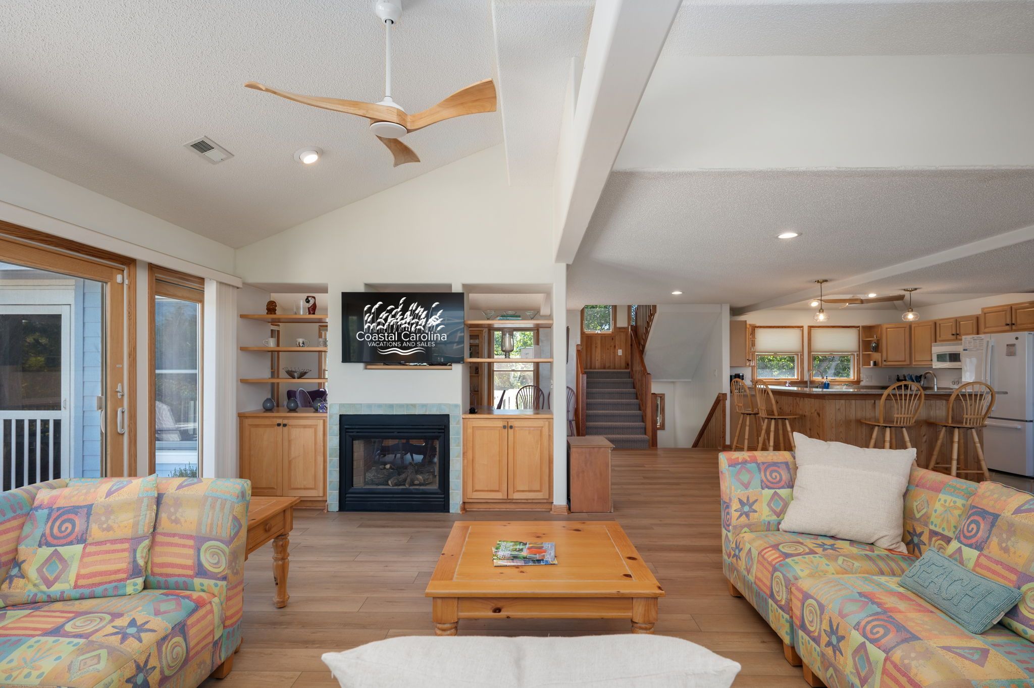 A spacious living room with a fireplace, wooden furniture, and a kitchen area with wooden cabinets and a dining table.