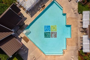 Ovenudblik over en swimmingpool med solterrasse, omgivet af liggestole og et afspærret område.