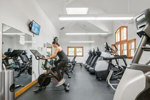 Un gimnasio con bicicletas estáticas y cintas de correr, un televisor montado en la pared y una ventana con luz natural.
