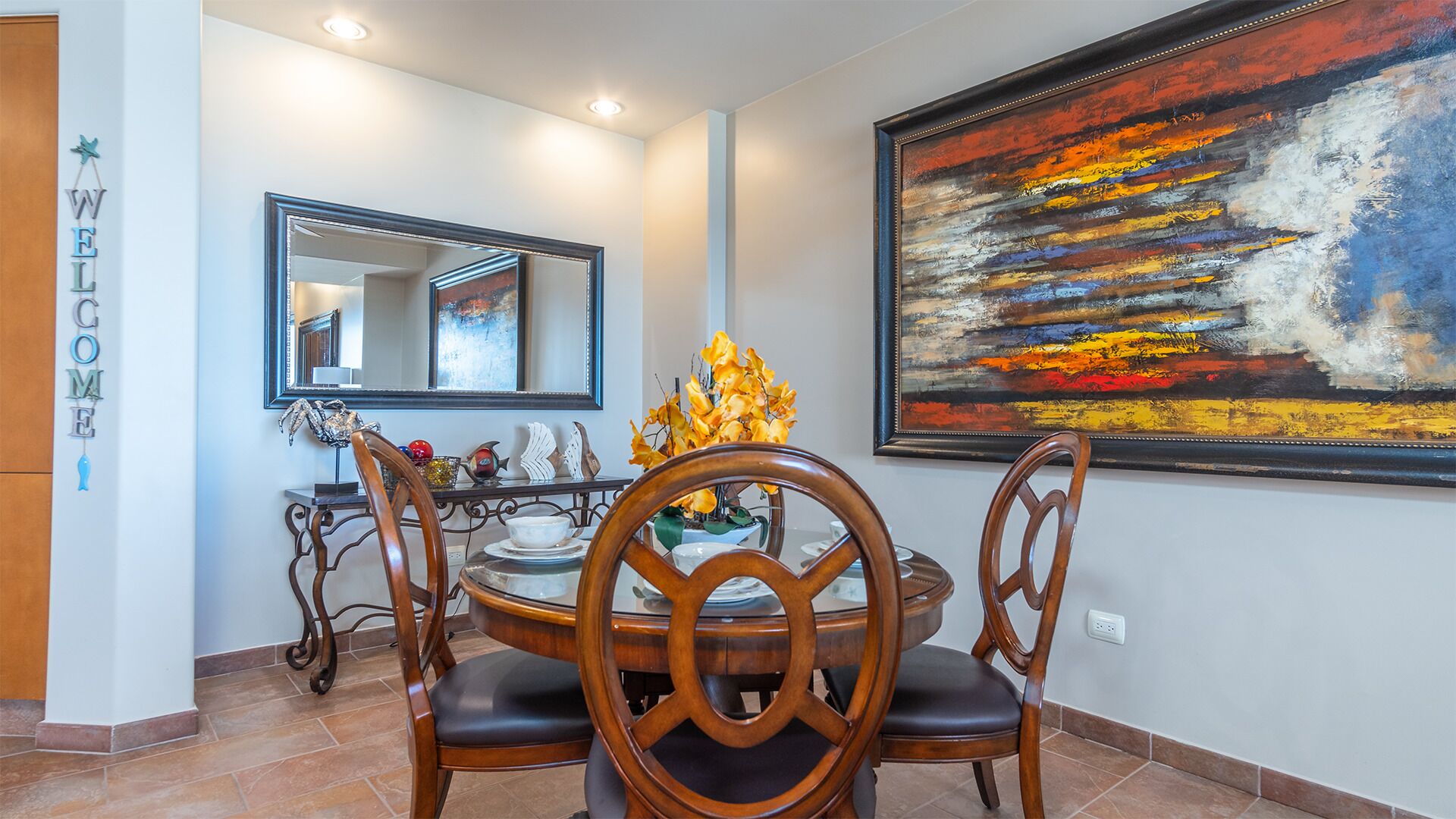 A dining area with a round table, chairs, a mirror, and a large abstract painting.