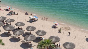 En strand med strandparasoller af strå, liggestole og en kiosk.