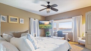 Habitación de hotel con una cama grande, ventilador de techo, televisor, escritorio y vistas al exterior.