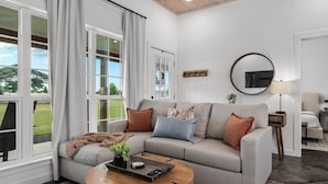 Ein modernes Wohnzimmer mit einem grauen Sofa, einem runden Couchtisch und einem großen Fenster mit Vorhängen.
