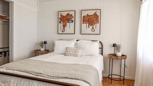 A bedroom with a bed, two nightstands, a wooden floor, and white walls.