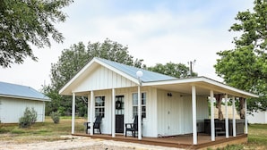 Une maison en bois blanche, avec une véranda, deux chaises et une table.
