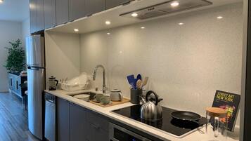 A modern kitchen with a stainless steel refrigerator, a built-in oven, a sink with a faucet, and a kettle on the stove.