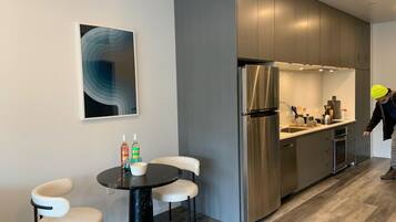 A modern kitchen with stainless steel appliances, a dining area with a round table and chairs, and a large abstract painting on the wall.