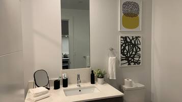 A modern bathroom with a large mirror, a sink, a toilet, and two abstract wall art pieces.