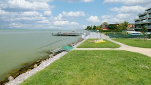 Une vue sur le lac, avec un quai, des zones herbeuses et des bâtiments en arrière-plan.