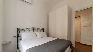 A single bed with a metal frame, white bedding, and a gray blanket. There is a white wall with a power outlet and a door to the right. - Testaccio 11 - FromHometoRome (Roma)