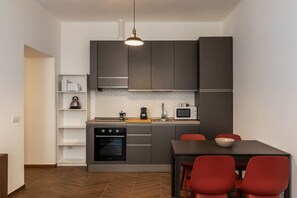 Een moderne keuken met grijze kastjes, een zwarte oven, een magnetron en een eettafel met rode stoelen.