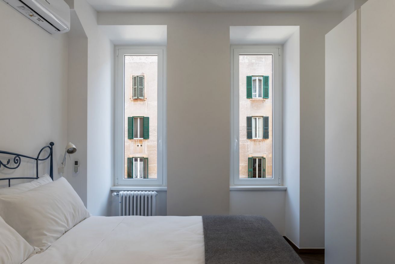 A bedroom with a bed, a radiator, and two windows with shutters.